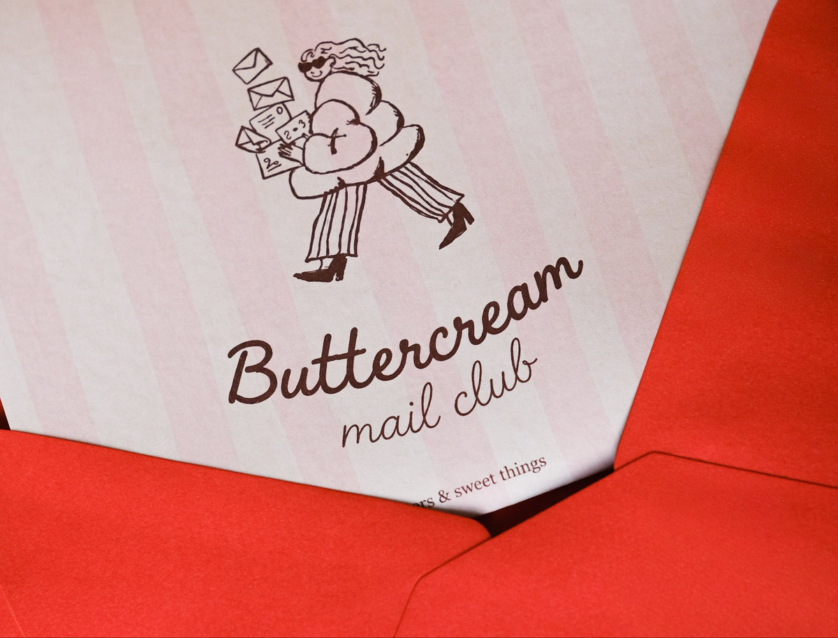 A red envelope with a striped Buttercream Mail Club card peeking out, reading letters and sweet things.